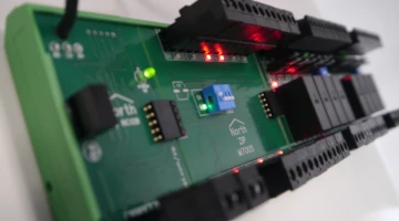 Close-up of a green North Zip M7005 modules showing active red and green LED indicators, terminal blocks, and a blue DIP switch address block.